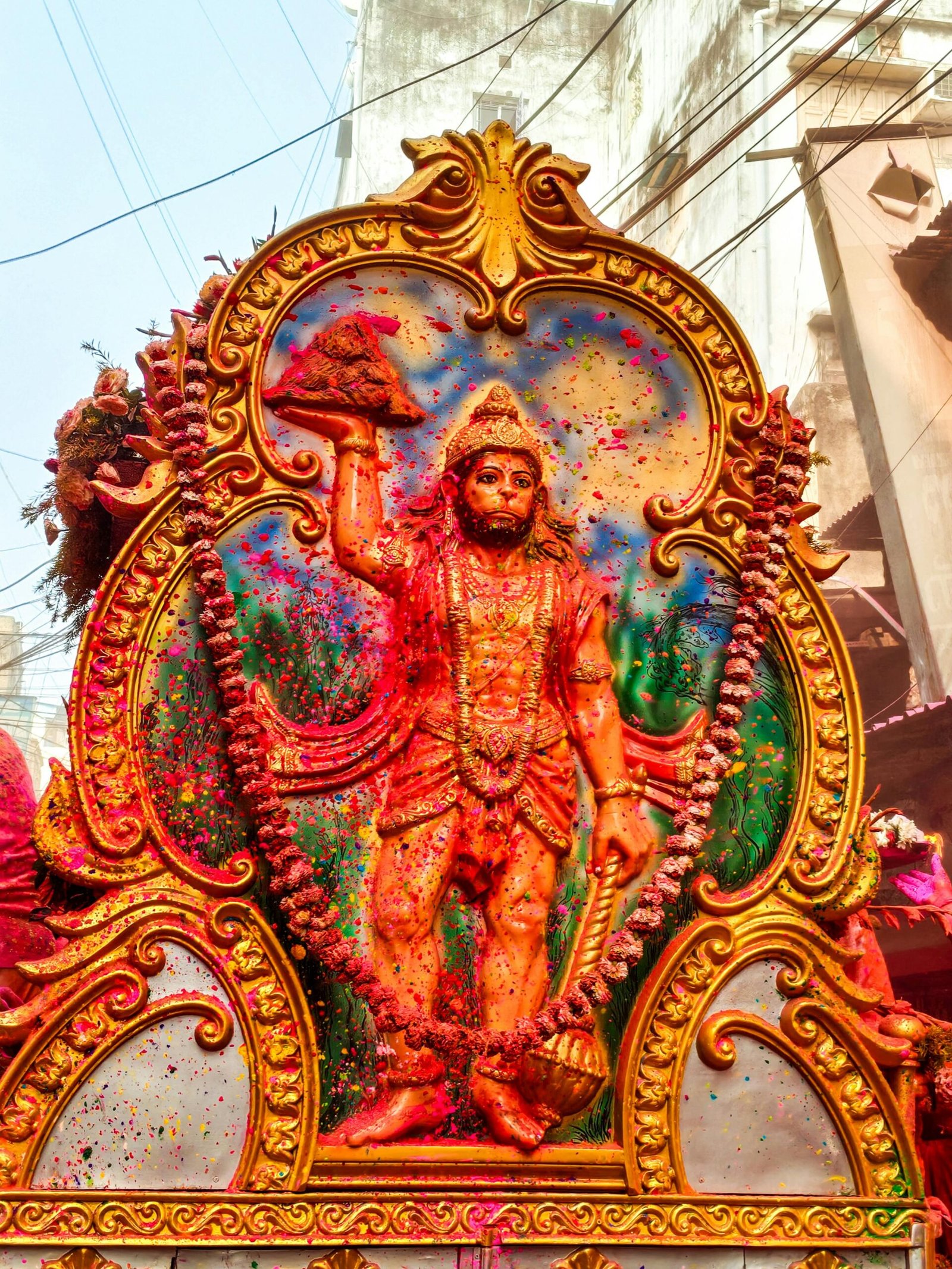 Vibrant Hanuman statue covered in powder colors during an Indian festival celebration.
